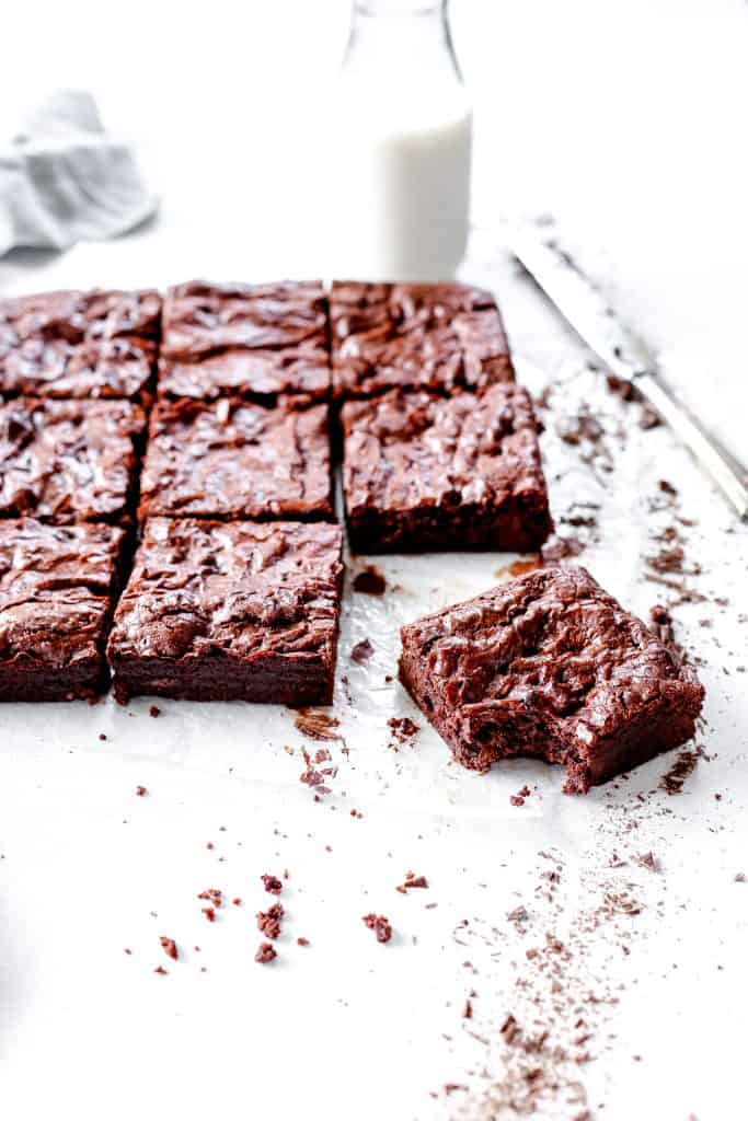 Brownie with a bite taken out of it on a white surface with more brownie squares.