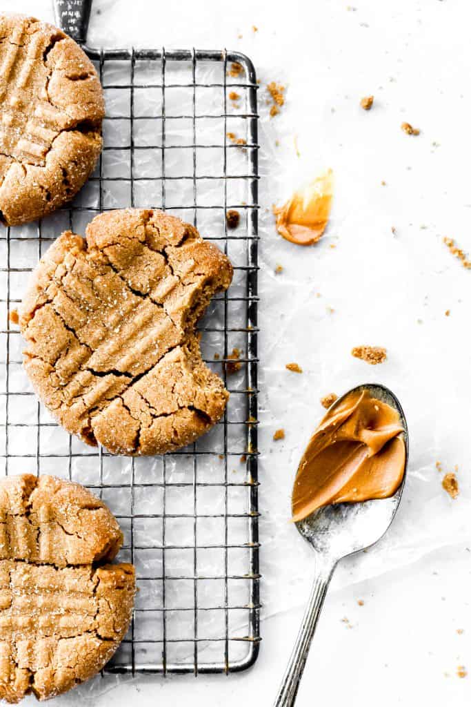 Vegan Peanut Butter Cookies on a wire rack and a spoon full of peanut butter.