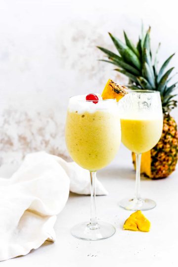 Two banana piña coladas in front of a whole pineapple.