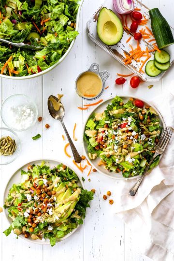 Two plate of vegan cobb salad, a big bowl of cobb salad and a cutting board with assorted veggies.