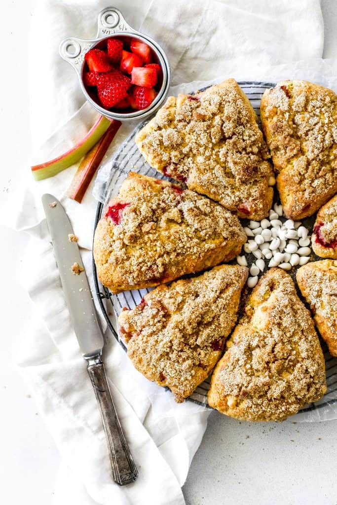 Vegan strawberry rhubarb scones on a wire cooling rack and a cup of strawberries.