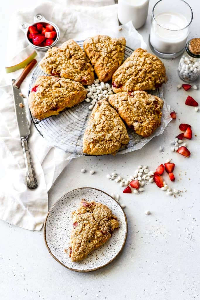 Vegan strawberry rhubarb scone on a plate and more scones behind it on a cooling rack.