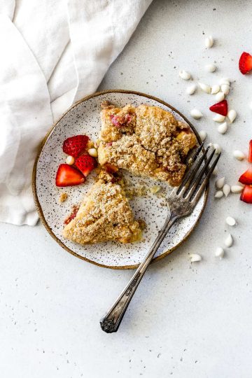 Vegan strawberry rhubarb scone cut in half on a plate with a fork.