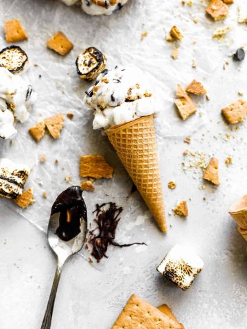 S'mores ice cream cone lying flat on a white surface next to a spoon covered in chocolate and graham cracker chunks.