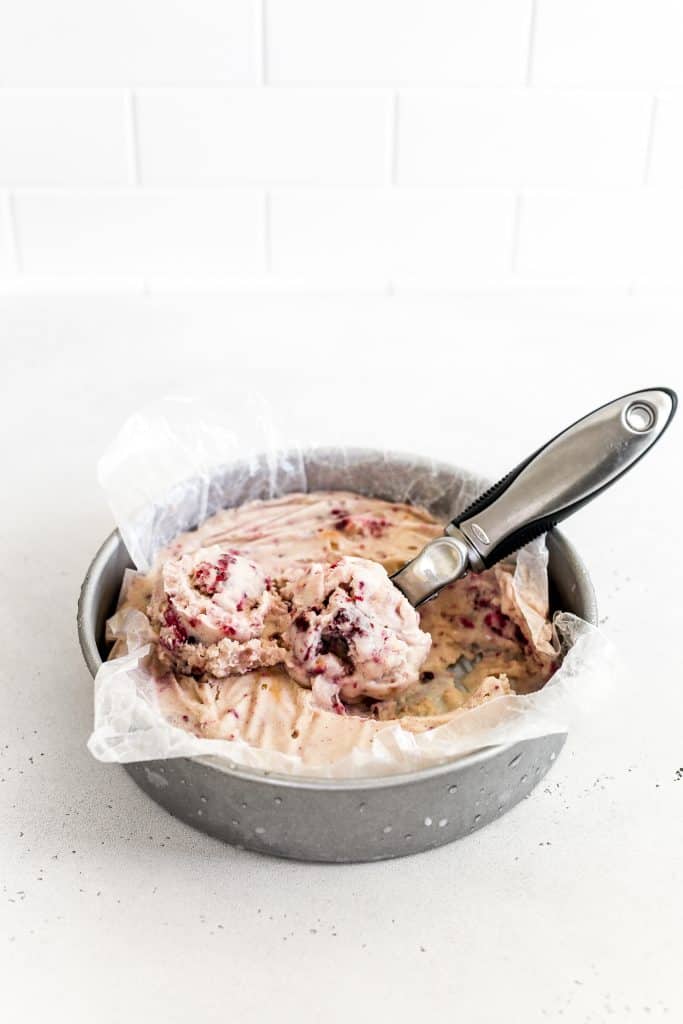 Vegan blackberry cobbler ice cream frozen in a round cake pan with an ice cream scoop full of ice cream.