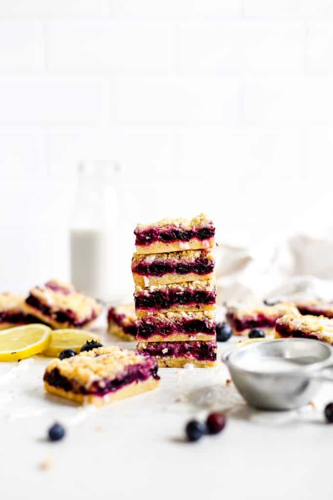 Stack of lemon blueberry bars in front of a jug of milk and a linen napkin.