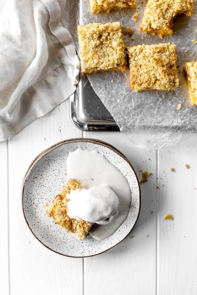 Vegan peach crumble bar on a plate covered in melted vanilla ice cream.