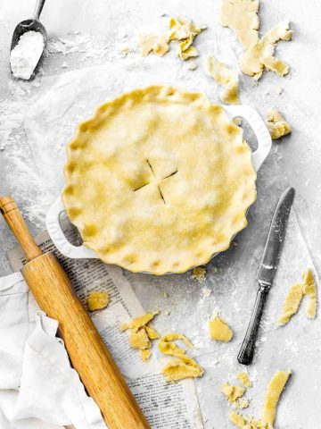 Unbaked pie next to pie crust scraps, a rolling pin and a knife.