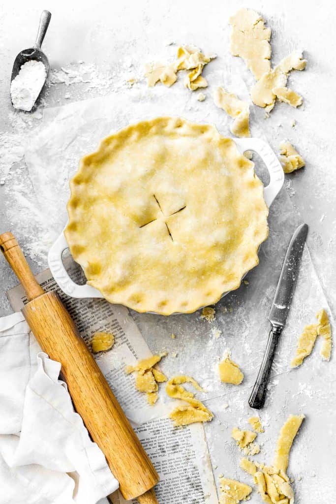 Unbaked pie next to pie crust scraps, a rolling pin and a knife.