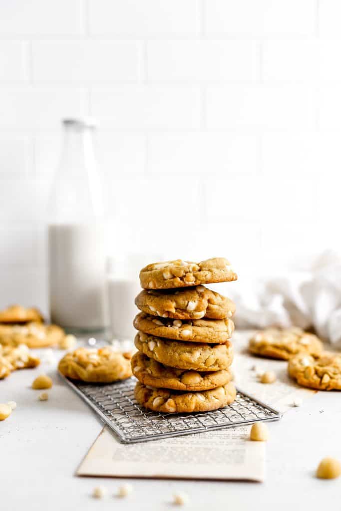 Stack of vegan white chocolate macadamia cookies on a wire rack and a jug of milk.