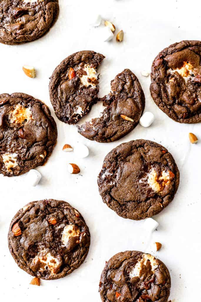 Vegan rocky road cookies on a white surface, one being pulled apart looking gooey.