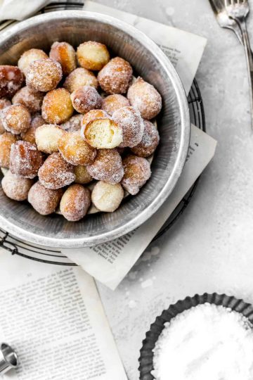 Pie pan filled with sugar-covered vegan donut holes, one with a bite taken out of it.