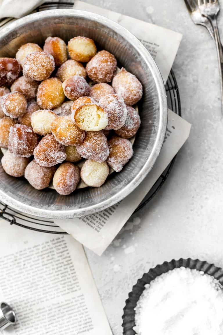 Pie pan filled with sugar-covered vegan donut holes, one with a bite taken out of it.