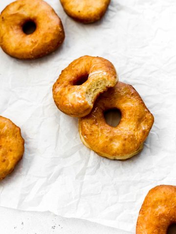 Glazed vegan donut with a bite taken out of it propped against another donut.