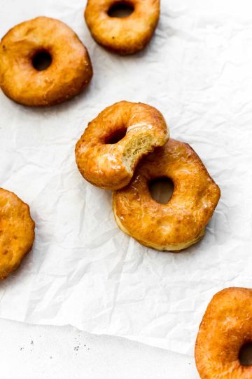 Glazed vegan donut with a bite taken out of it propped against another donut.