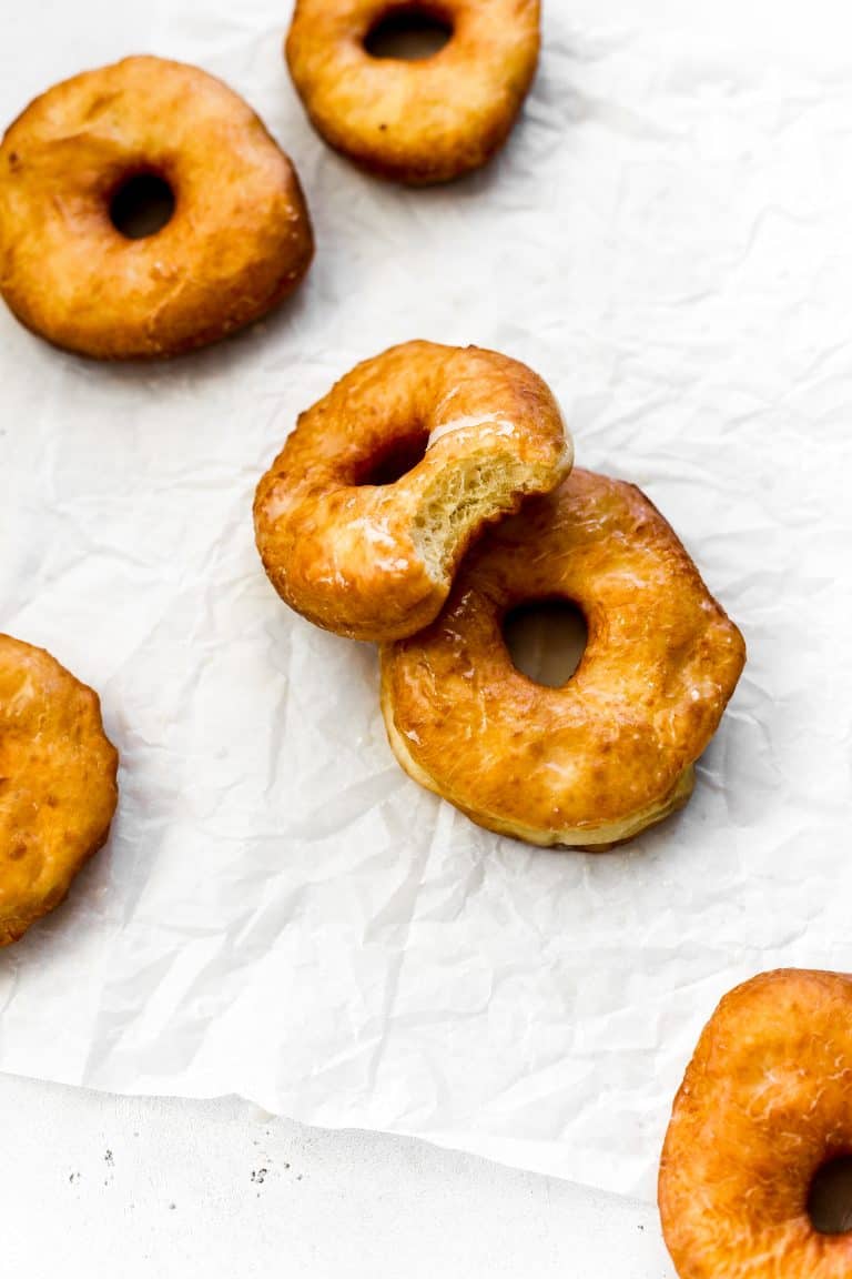 Glazed vegan donut with a bite taken out of it propped against another donut.