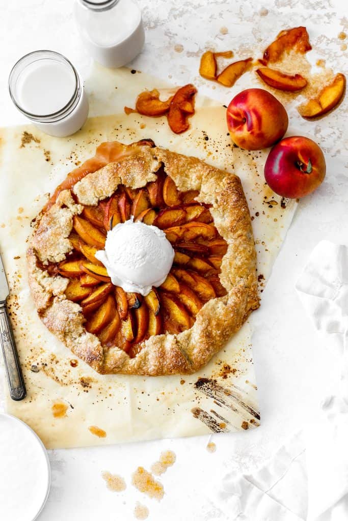 Vegan nectarine galette topped with a scoop of vanilla ice cream, a glass of milk and two nectarines.