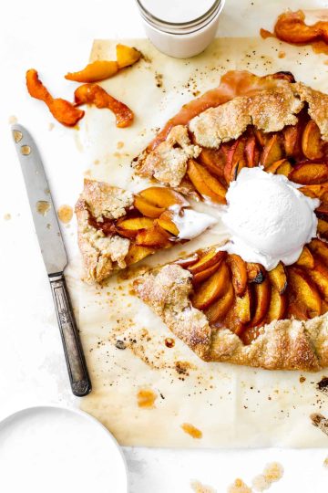 Slice of nectarine galette being pulled out of the whole galette topped with vanilla ice cream and a knife.