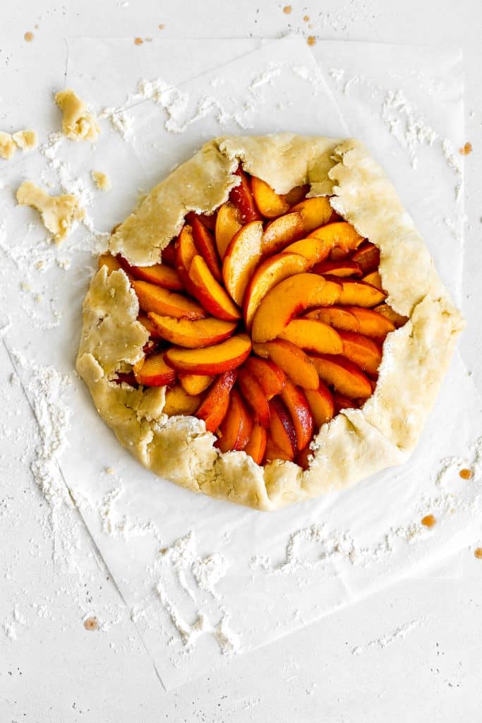 Unbaked vegan nectarine galette sitting on white parchment paper.