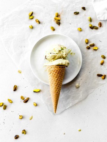 Vegan pistachio ice cream can lying on a white plate surrounded by scattered pistachios.