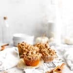 Vegan pumpkin muffin on a wire cooling rack with its wrapper pulled down in front of a jug of milk and a stack of white plates.