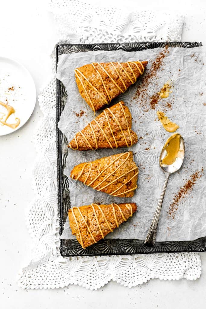 Four vegan pumpkin scones arranged on a baking sheet surrounded by scattered ground cinnamon.