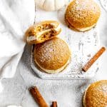 Vegan pumpkin whoopie pie with a bite taken out of it on a white cutting board.