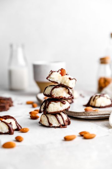 Close of of a stack of vegan almond joys bites in front of a jar of almonds and a jug of milk.