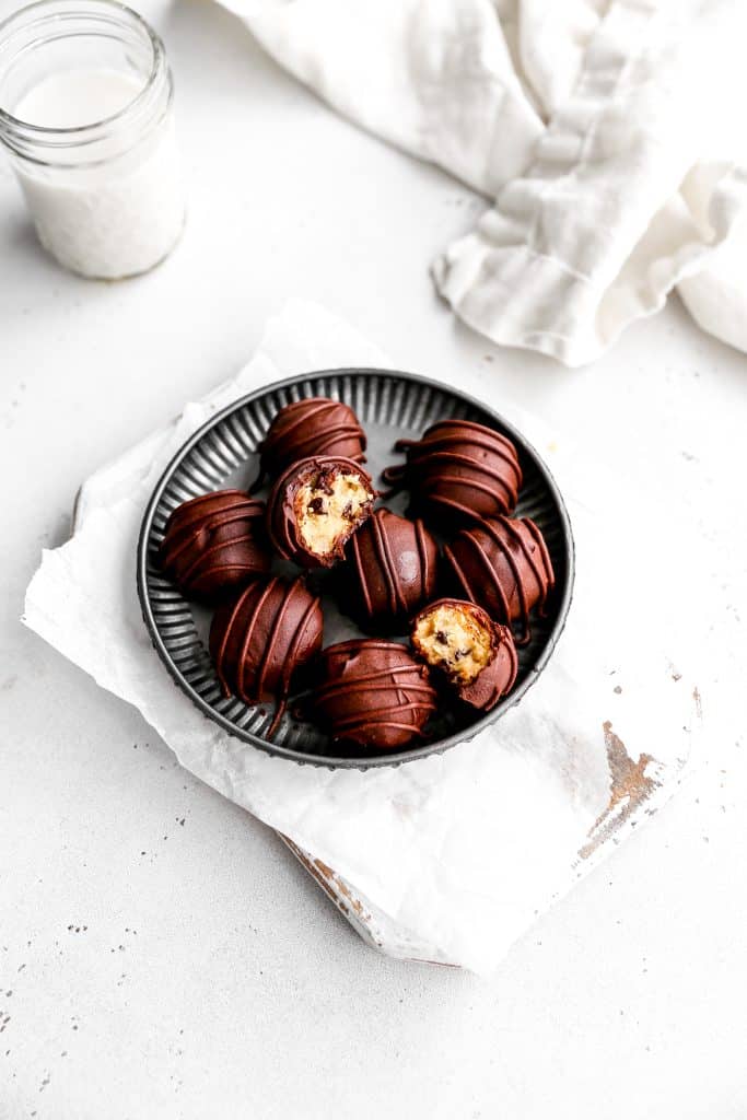 Vegan cookie dough bites on a silver plate next to a linen napkin and a glass of milk.