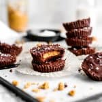 Vegan peanut butter cup with a bite taken out of it stacked on top of another peanut butter cup on a baking sheet in front of a jar of peanut butter and a jug of milk.