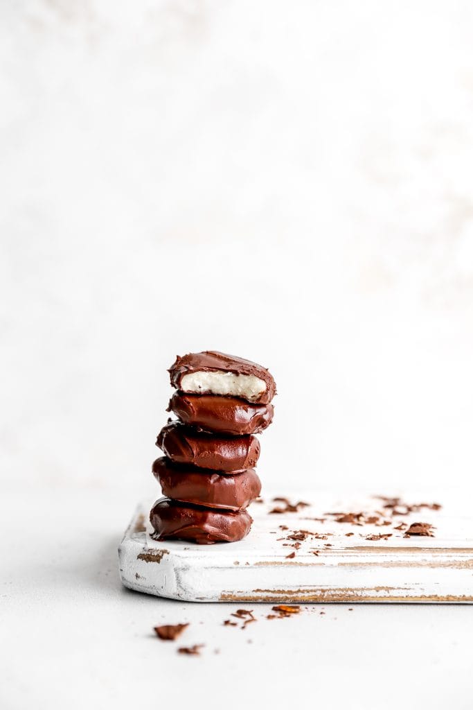 Vegan peppermint patty with a bite taken out of it on top of a stack of additional patties on a white wooden cutting board.