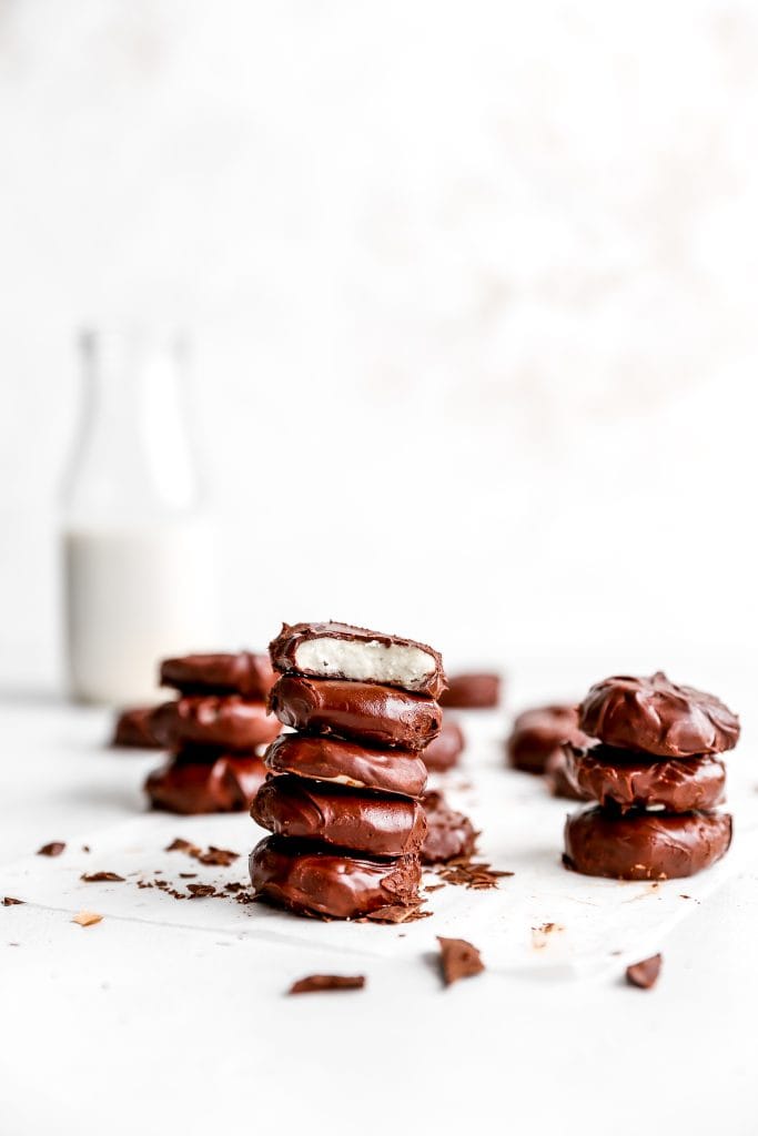 Vegan peppermint patty with a bite taken out of it on top of a stack of more peppermint patties in front of additional stacks and a jug of milk.