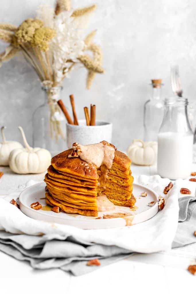 Close up showcasing internal view of stack of vegan pumpkin pancakes topped with oozing cinnamon butter and pecans.