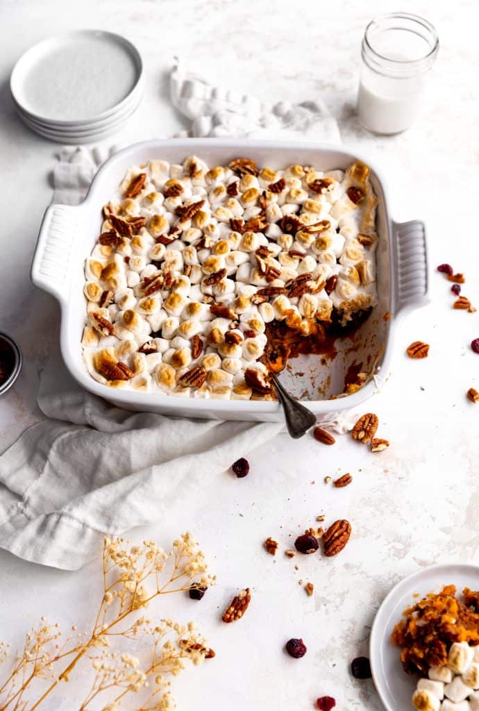 Serving spoon in a dish of vegan sweet potato casserole next to a white plate holding a serving.