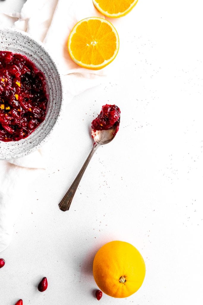 Spoon filled with orange cranberry sauce surrounded by oranges and orange slices.