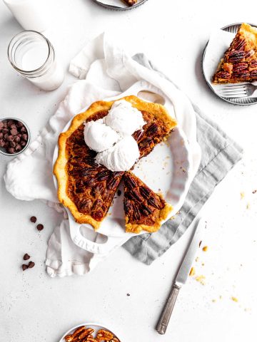 Vegan chocolate bourbon pecan pie with slices missing. Pie is topped with ice cream surrounded by slices of pie on plates.