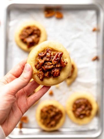 Hand holding a vegan pecan pie cookie over a baking sheet with more cookies.