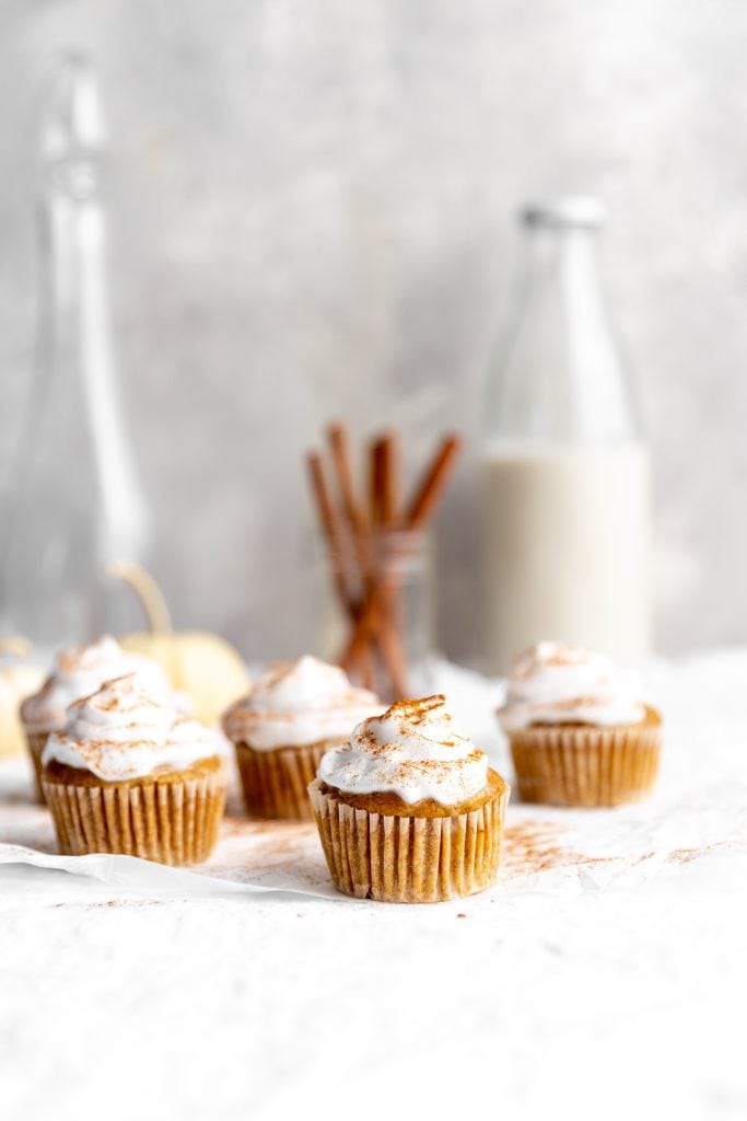 Vegan pumpkin pie cupcakes in front of a jar of cinnamon sticks and a jug of milk.