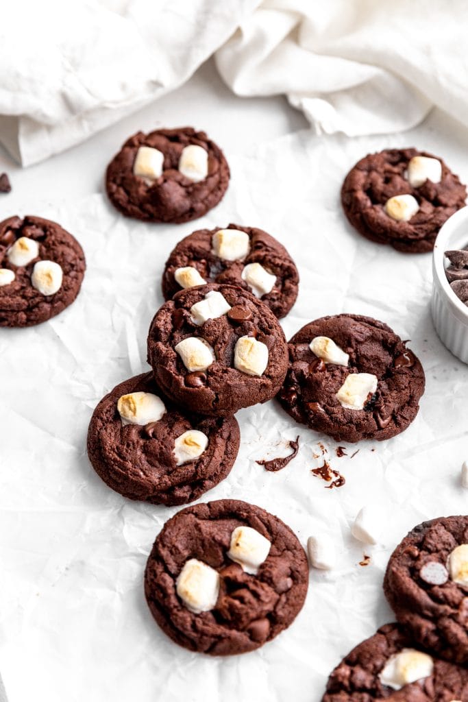 Vegan hot chocolate cookies in front of a white linen napkin next to a cup of chocolate chips.