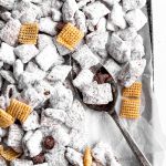 Spoon stirring up vegan muddy buddies on a baking sheet.