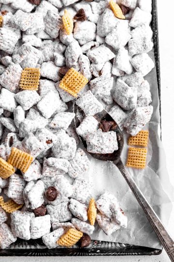 Spoon stirring up vegan muddy buddies on a baking sheet.