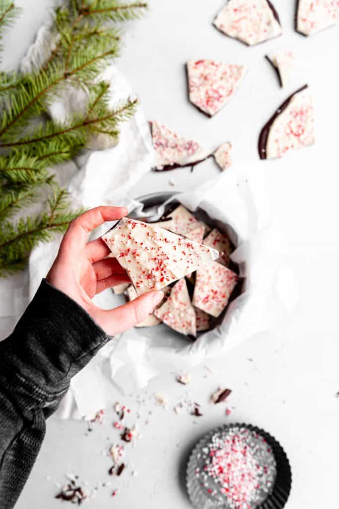 Hand holding a piece of vegan peppermint bark over a pan filled with more bark.