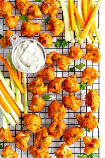 Buffalo cauliflower on a wire cooling rack with carrot sticks, celery sticks and a cup of ranch dressing.
