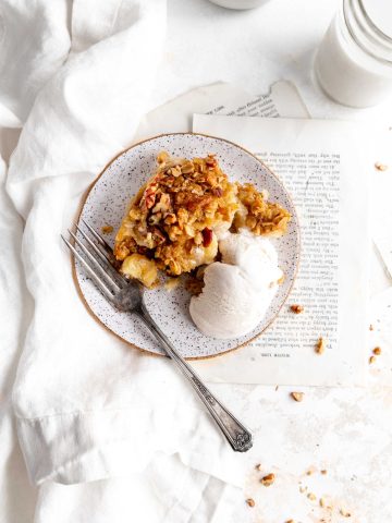 Plate of vegan banana cobbler and vanilla ice cream next to a glass of milk and a white linen napkin.