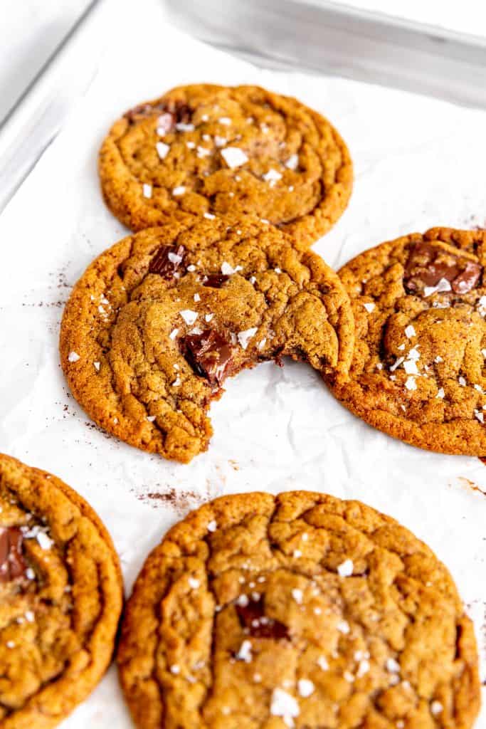 Vegan espresso chocolate chip cookie with a bite taken out of it propped against other cookies.