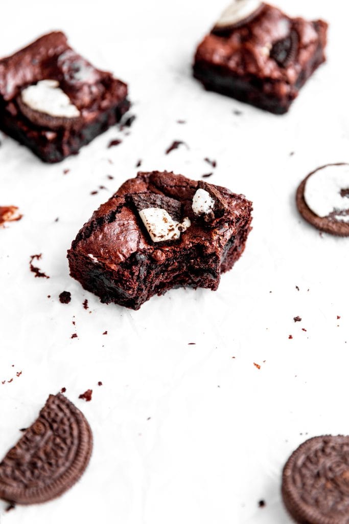 Vegan oreo brownie with a bite taken out of it surrounded by more brownies and oreo cookie pieces.