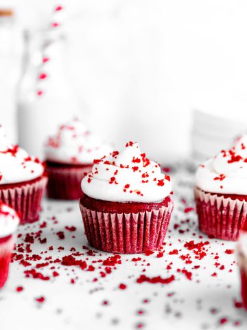 Vegan red velvet cupcakes topped with red velvet cake crumbs surrounded by more cupcakes.