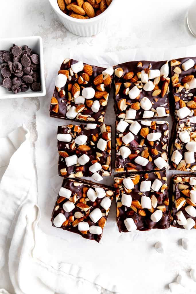 Vegan rocky road bars laid out on a white surface next to a cup of chocolate chips.