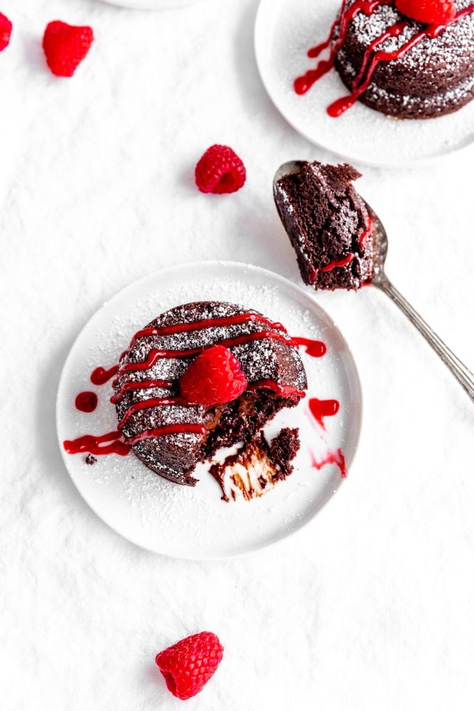 Chocolate lava cake drizzled with raspberry sauce on a white plate next to a spoonful of cake.