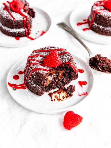 Half of a lava cake oozing chocolate sauce in front of two more plates of cake.